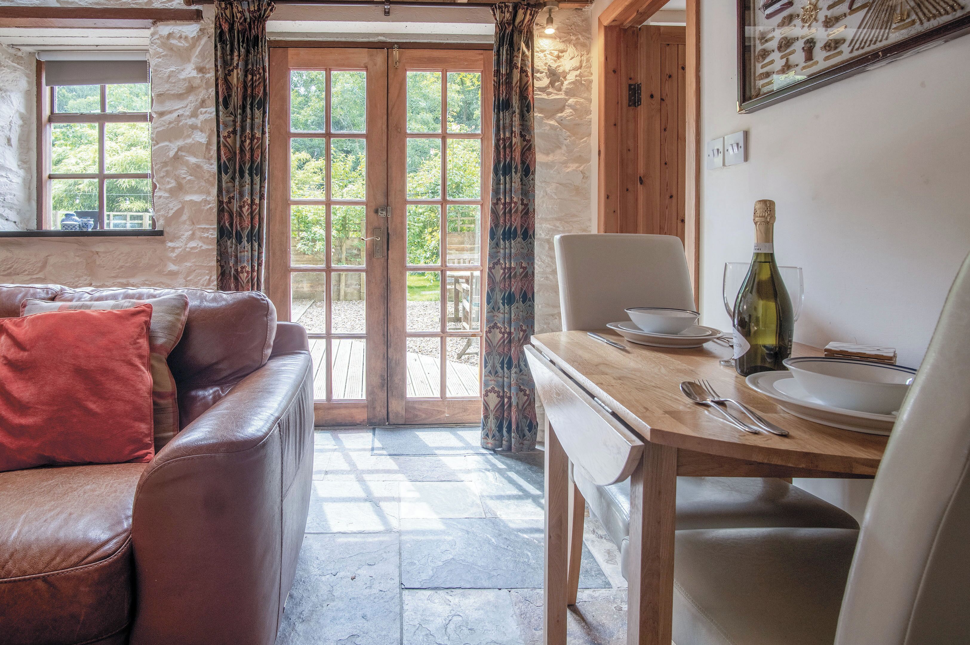 A cozy room with a leather sofa, a wooden dining table set with plates, a bottle of wine, and a chair.