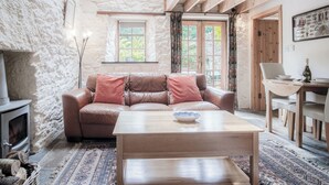 A cozy living room with a stone wall, a leather sofa, a wooden coffee table, and a fireplace.