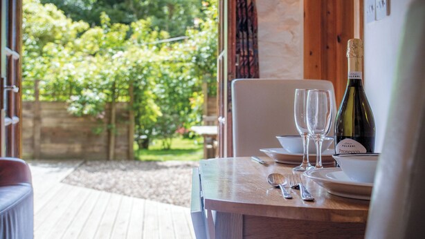 A wooden table with a bottle of Prosecco, two wine glasses, and dining utensils.