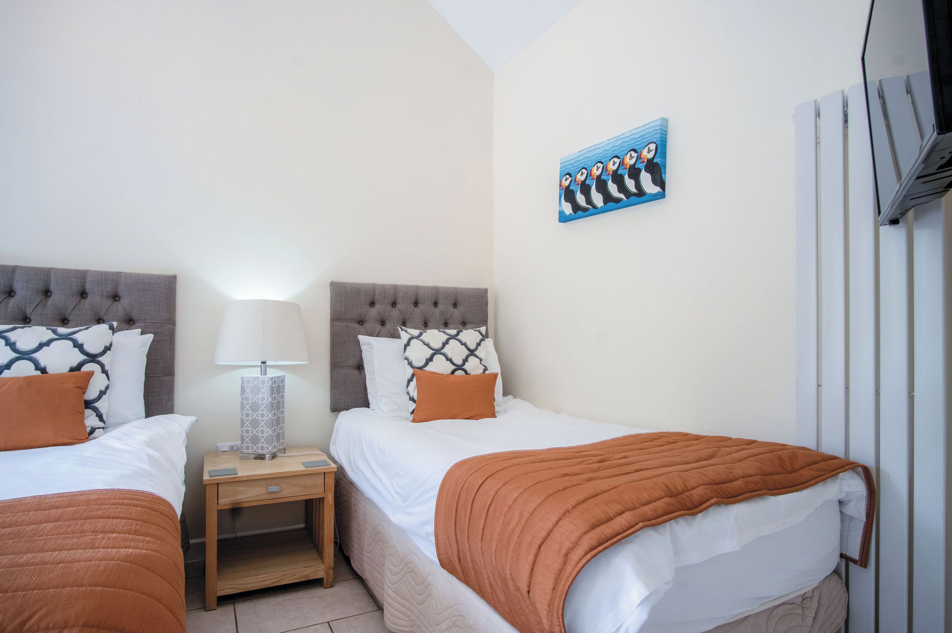 Een hotelkamer met twee bedden, een nachtkastje met een lamp en een aan de muur hangend kunstwerk.