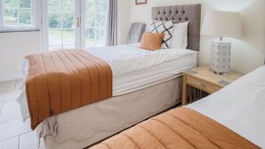 A bedroom with two beds, a nightstand, a lamp, and a window with a view of greenery. - Ysfael - 1 Bedroom Studio - St Ishmael's (Haverfordwest)