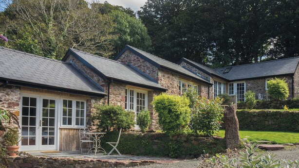 A stone building with a sloped roof, a wooden door, and a small patio area with a chair and table. - Ysfael - 1 Bedroom Studio - St Ishmael's (Haverfordwest)