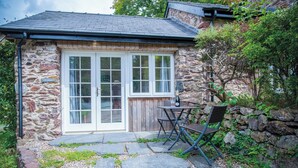 A stone cottage with a wooden deck, a small table with chairs, and a stone wall. - Ysfael - 1 Bedroom Studio - St Ishmael's (Haverfordwest)