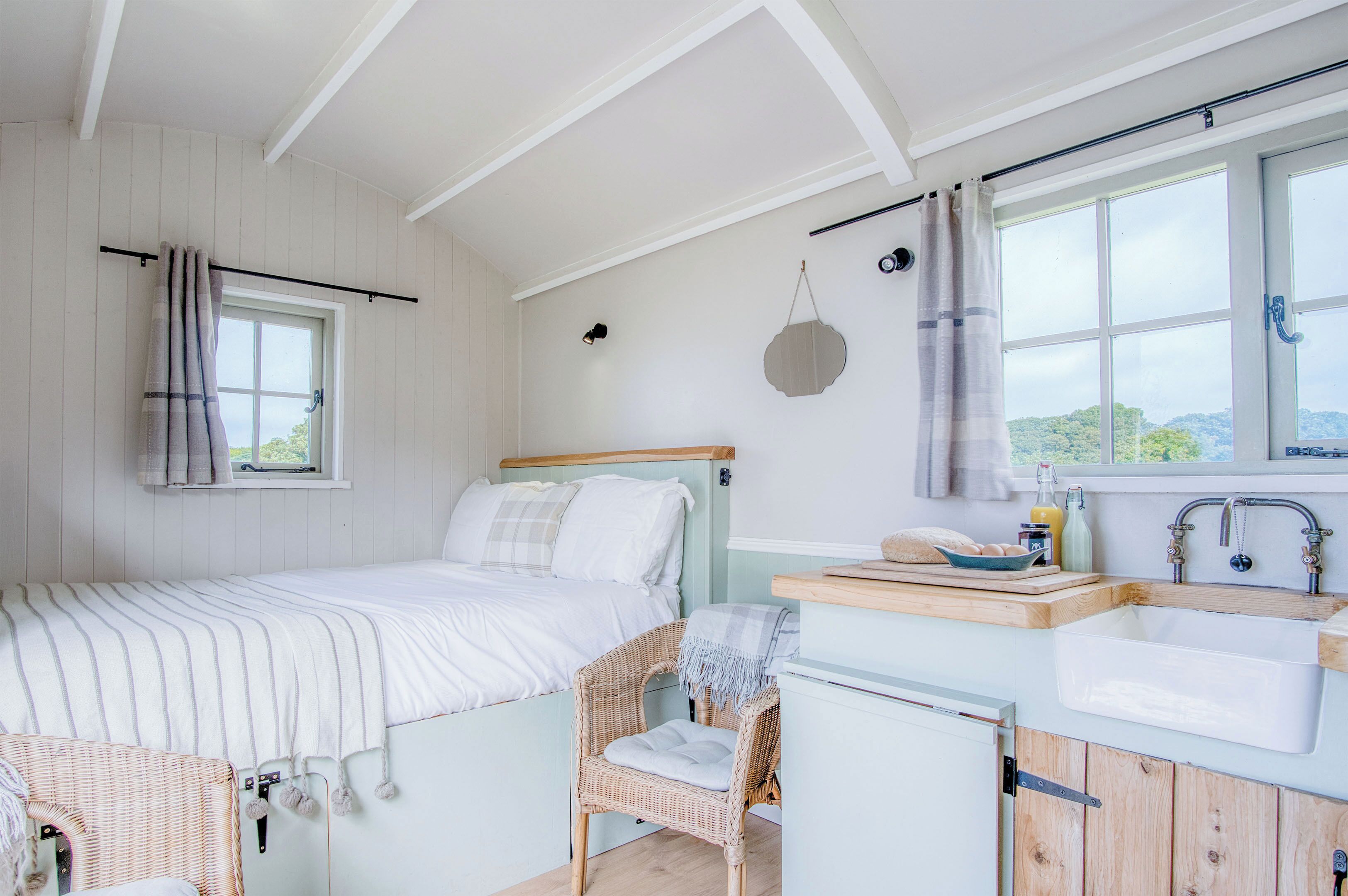 A bedroom with a bed, a chair, a window, a sink, and a view of the outdoors.