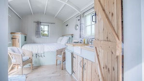 Een gezellige slaapkamer met een bed, twee rieten stoelen, een klein houten kastje en een raam met gordijnen.