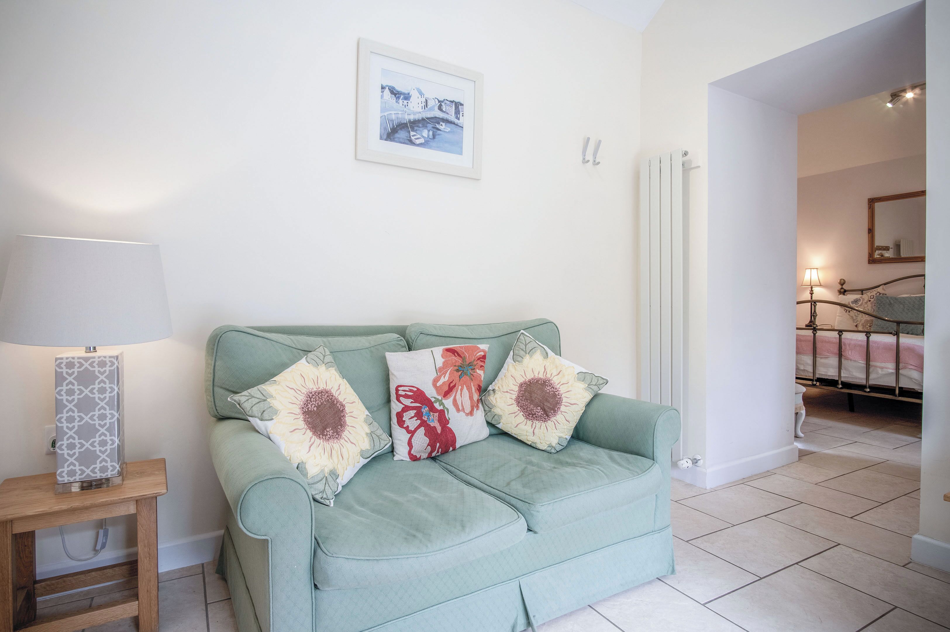 A living room with a green sofa, a side table with a lamp, and a framed picture on the wall.