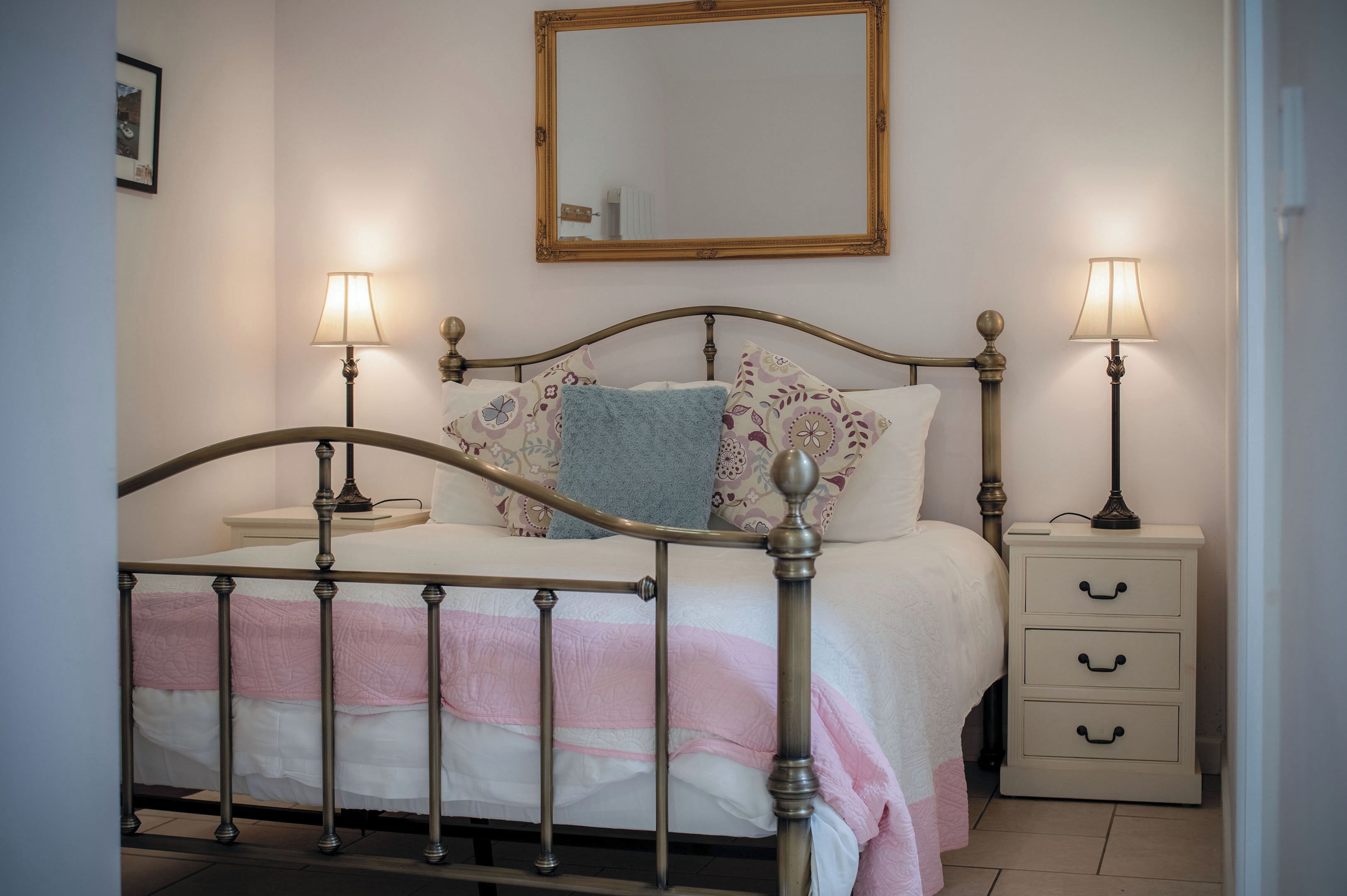 Un dormitorio con una cama, mesitas de noche, un tocador, un espejo y una lámpara.