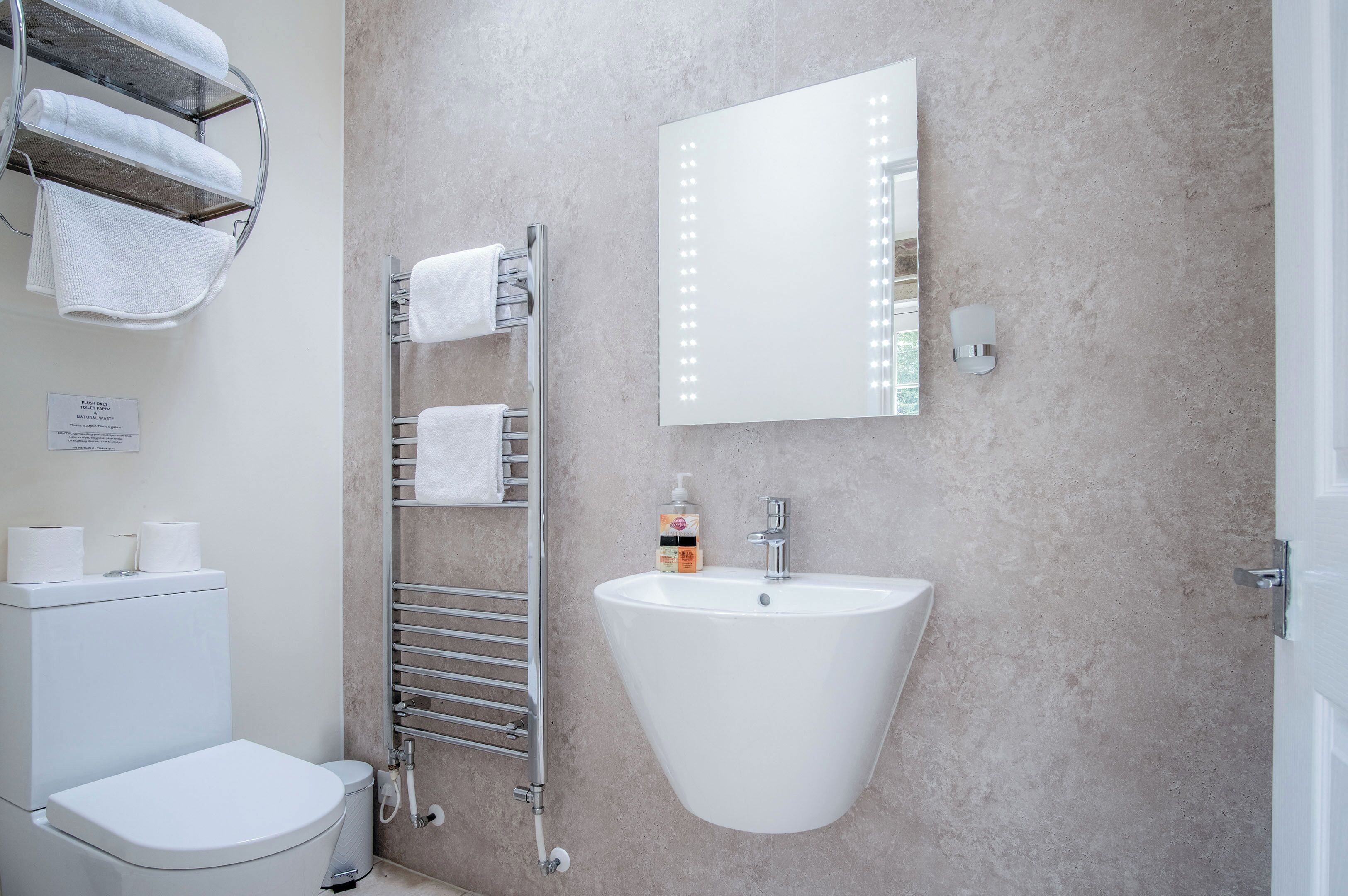 Un baño con un lavamanos blanco, un espejo con iluminación, un perchero para toallas y un inodoro.