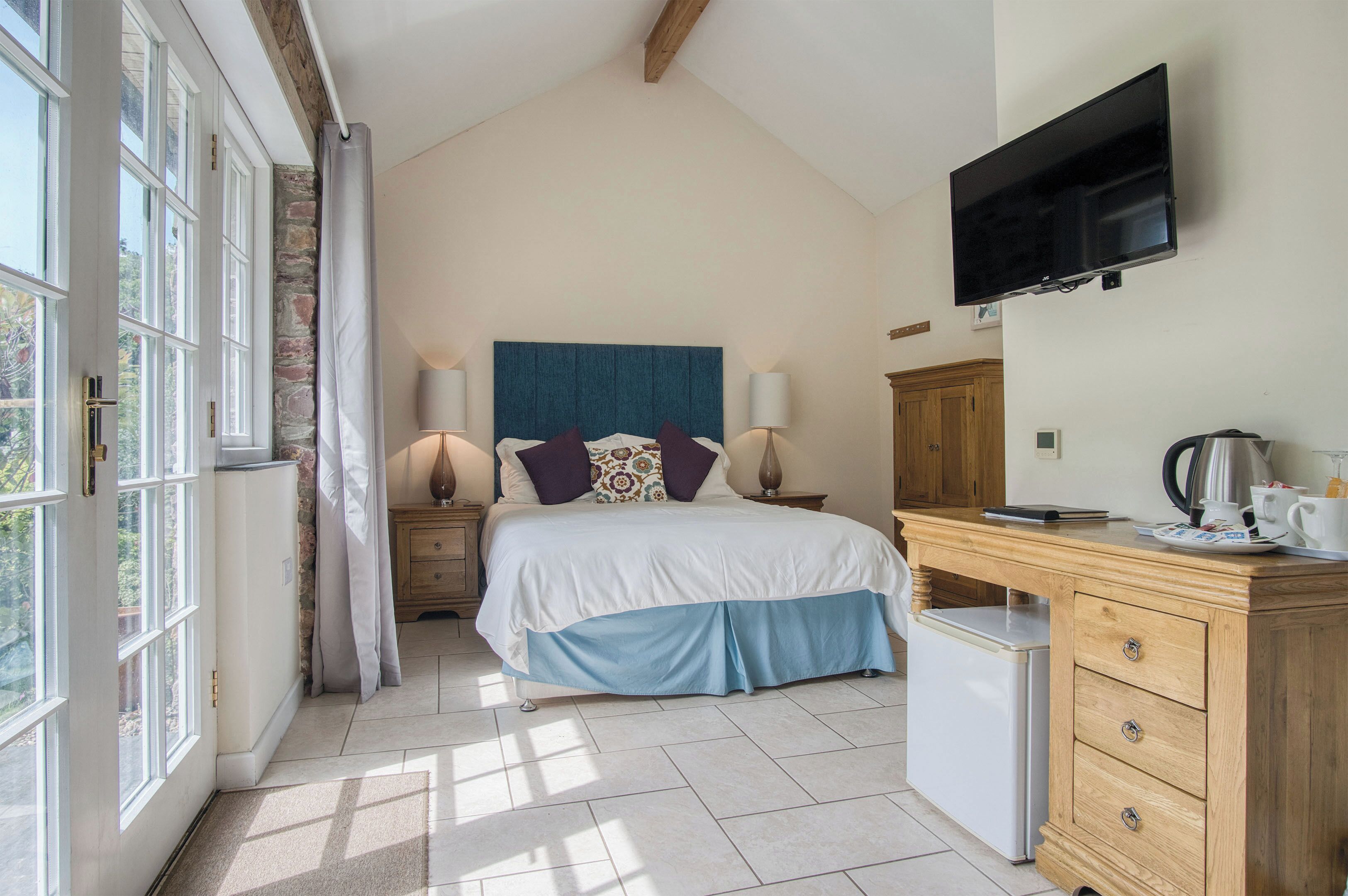 Een slaapkamer met een bed, bedlampen, een televisie, een bureau met een waterkoker en een koelkast.