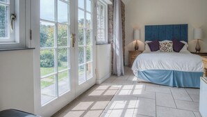 Une chambre avec une grande fenêtre, un lit recouvert d’une couvre-lit bleue et blanche, deux lampes de chevet et une vue sur la verdure à l’extérieur.