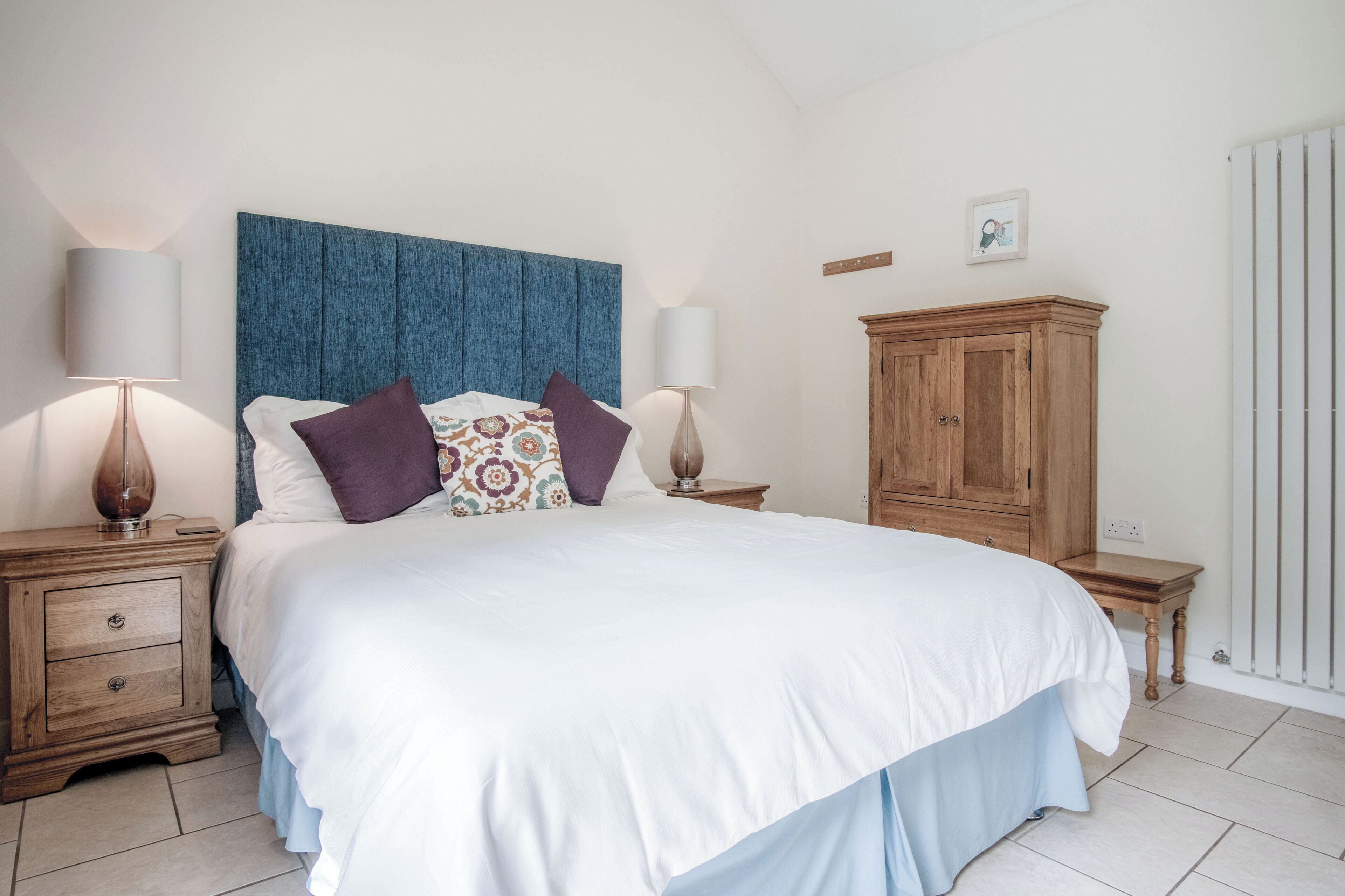 A bedroom with a large bed, wooden nightstands, a blue headboard, and a wooden cabinet.