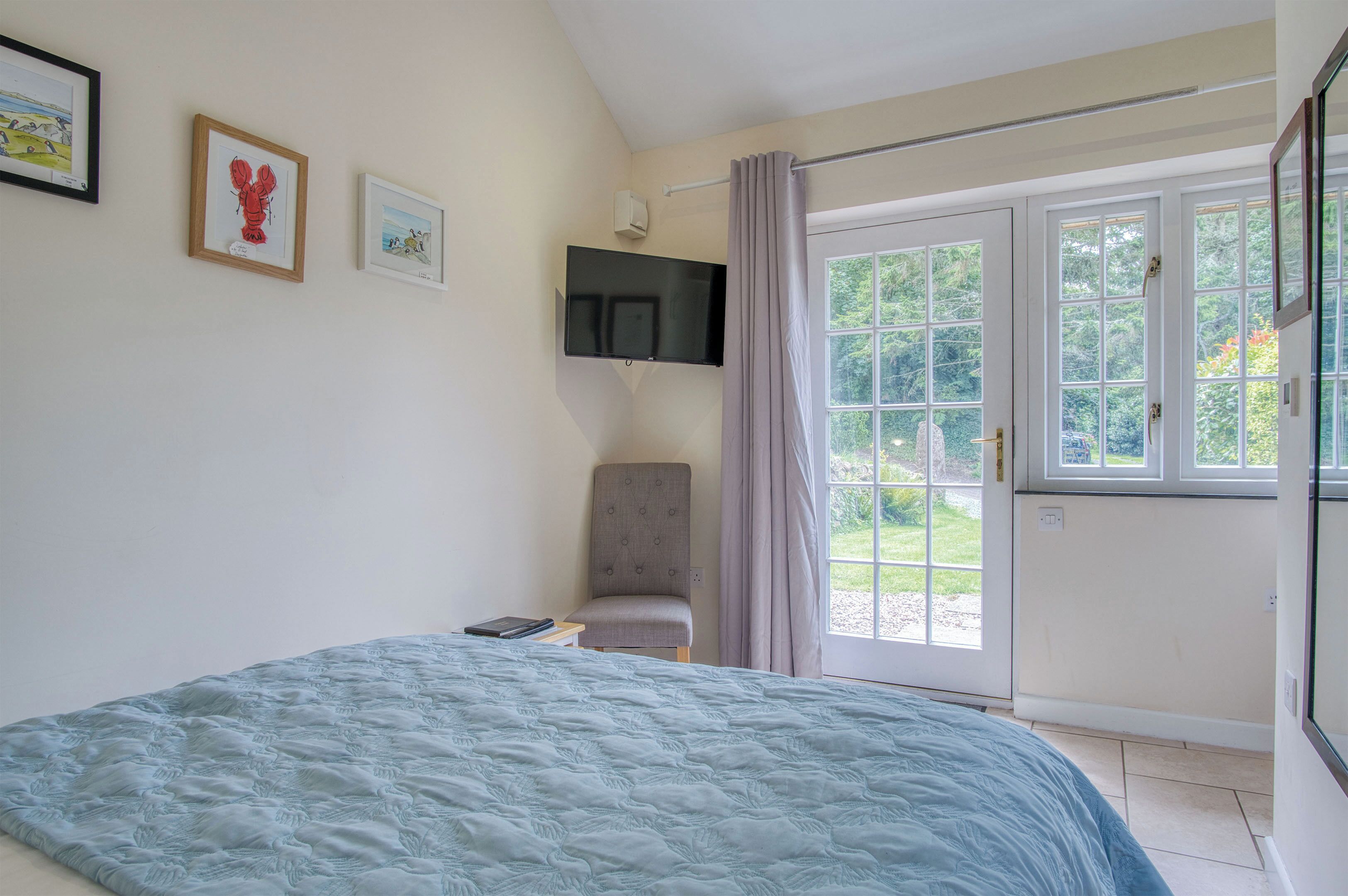 A bedroom with a bed, a chair, a TV, and a sliding glass door to a garden.