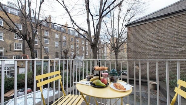 Een balkon met een gedekte tafel, inclusief fruit en gebak, en uitzicht op woongebouwen.