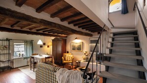A rustic interior with exposed wooden beams, a checkered sofa, a dining table, and a staircase. - La Colombaia romantic apartment (Margine Coperta-traversagna)