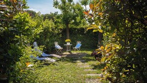An outdoor seating area with two white metal chairs and a small round table, surrounded by lush greenery and trees. - La Colombaia romantic apartment (Margine Coperta-traversagna)