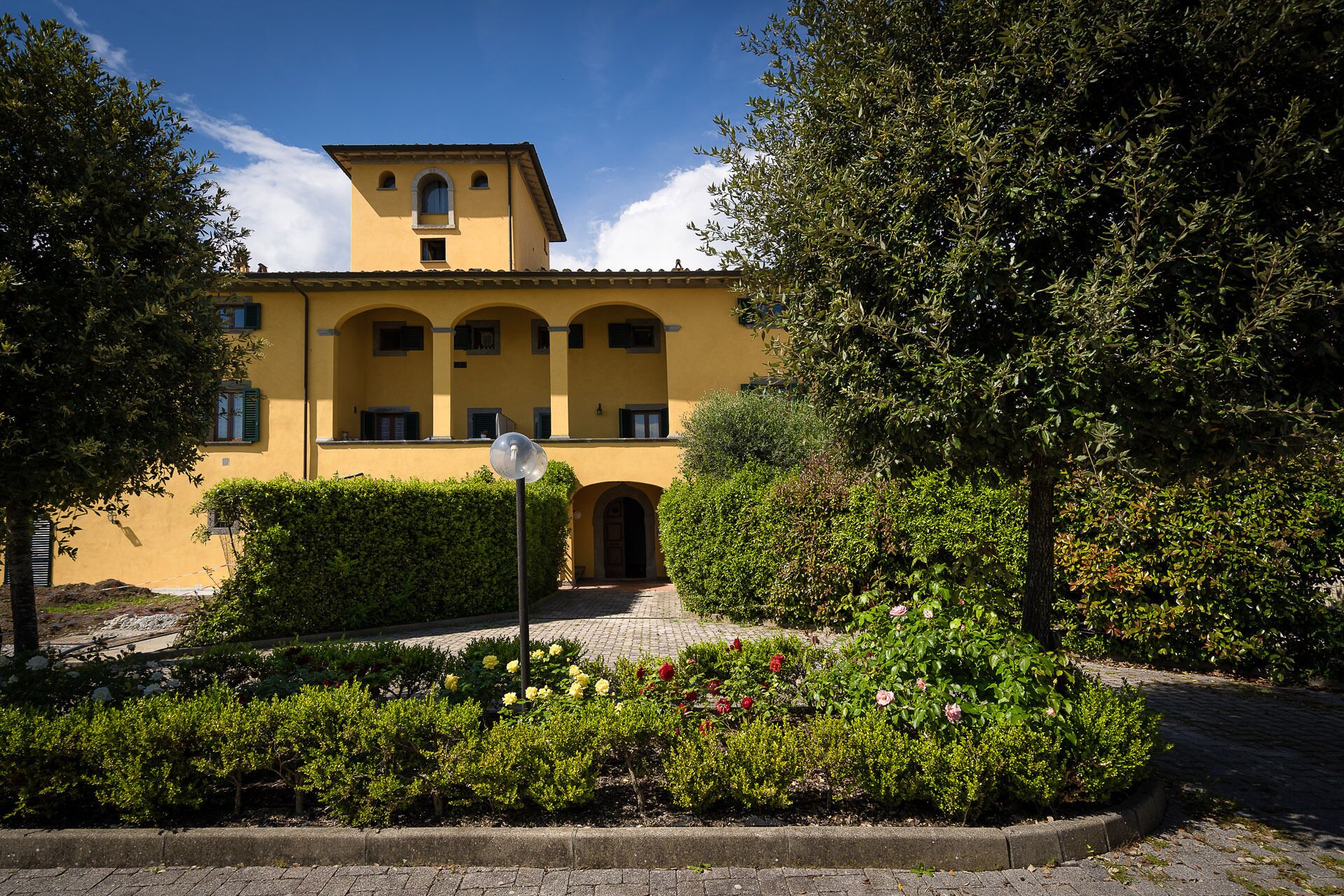 Un edificio giallo con un ingresso centrale, circondato da giardini curati e alberi.