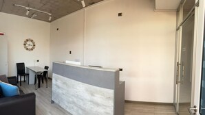A modern reception area with a curved desk, a clock on the wall, and a seating area with a couch and chairs. - Vistara Suites (Iquique)