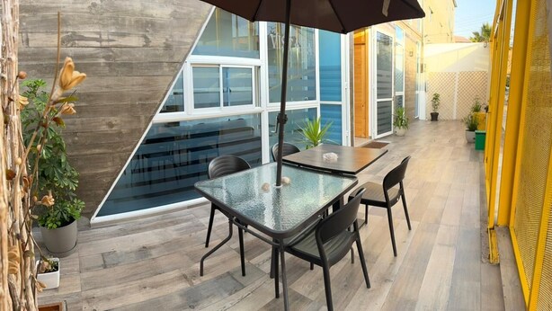 A modern patio with a glass table and chairs, surrounded by potted plants and a wooden floor. - Vistara Suites (Iquique)