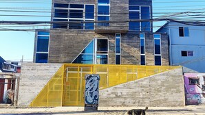 A modern building with a unique geometric design, featuring large windows and a prominent yellow section. - Vistara Suites (Iquique)