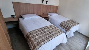 A room with two beds, a wooden headboard, a nightstand, and a wall-mounted light fixture. - Vistara Suites (Iquique)