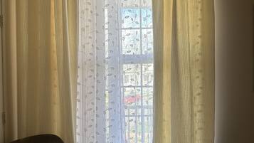 A room with a window covered by sheer curtains with a leaf pattern, a brown leather chair, and a bed with a floral bedspread.