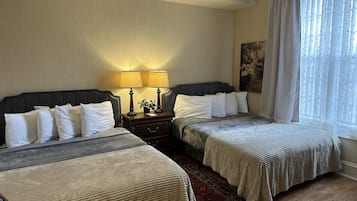 A hotel room with two beds, a nightstand with lamps, a painting on the wall, and a window with sheer curtains.