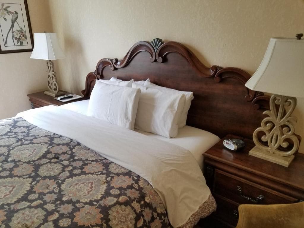 A neatly made bed with white linens, a patterned bedspread, and a wooden headboard. There are two bedside tables with lamps and a small decorative item on one.