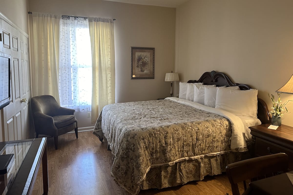 A hotel room with a bed, a chair, a desk, and a window with curtains.