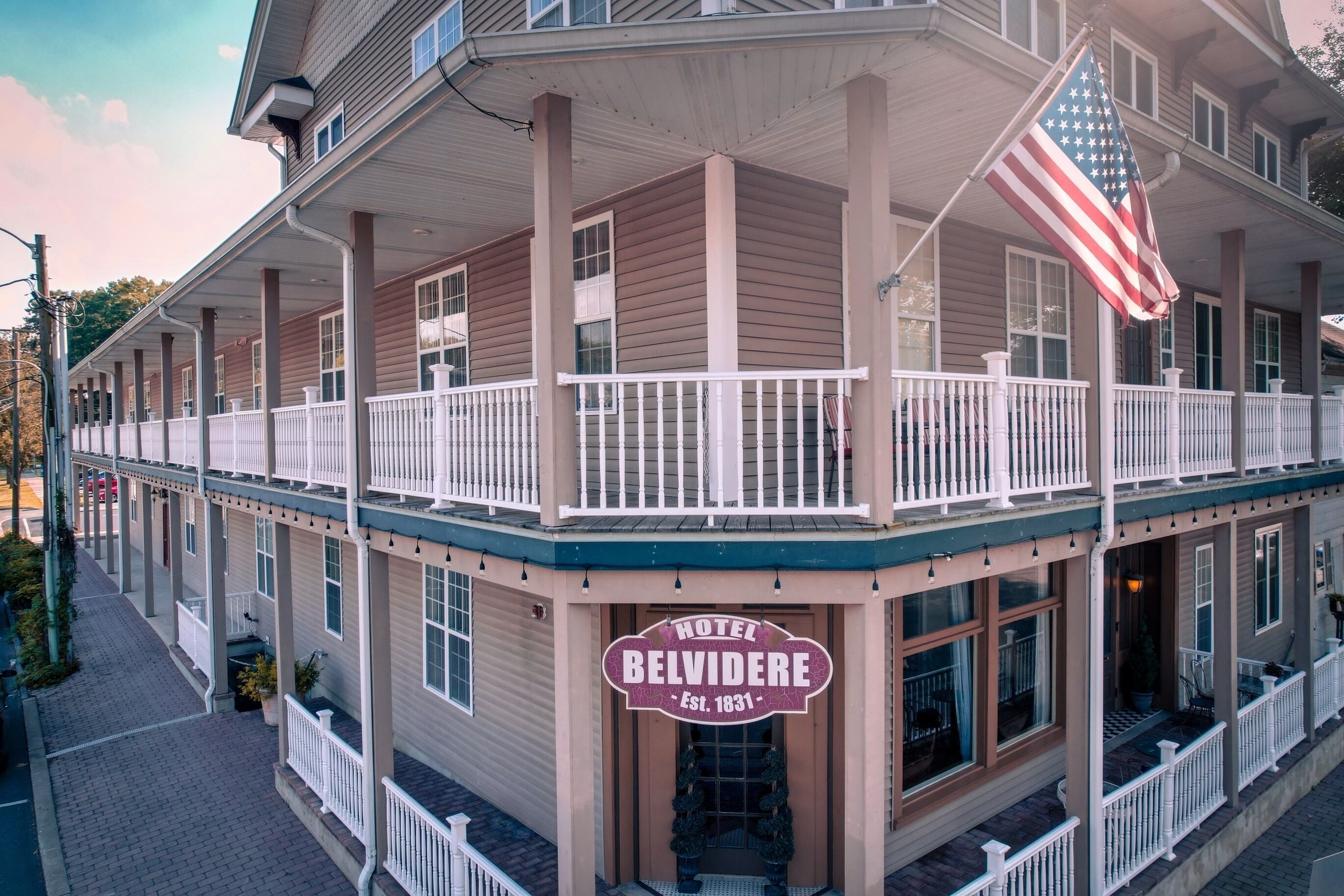 A historic hotel with a balcony, an American flag, and a sign stating "Hotel Belvidere Est. 1831".
