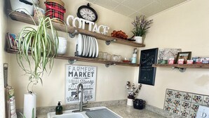 A kitchen with a granite countertop, a sink, and a stove. There are shelves with various items and a sign that reads "Farmers Market."