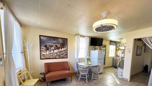 A cozy living room with a sofa, a dining table with chairs, a TV, and a kitchen area with a refrigerator and microwave.