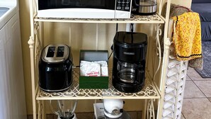 A kitchen with a white metal shelf holding a microwave, toaster, blender, coffee maker, and a mixer.