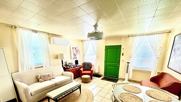 A living room with a sofa, a dining table with placemats, a green door, and a ceiling fan.
