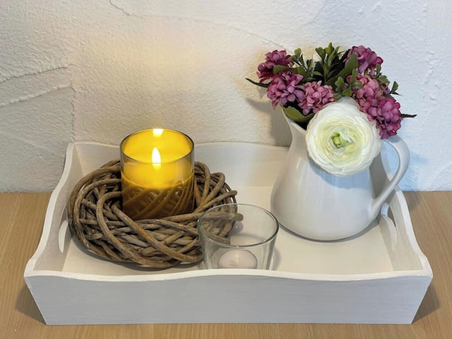 A white tray with a lit candle, a glass, and a white pitcher with flowers.