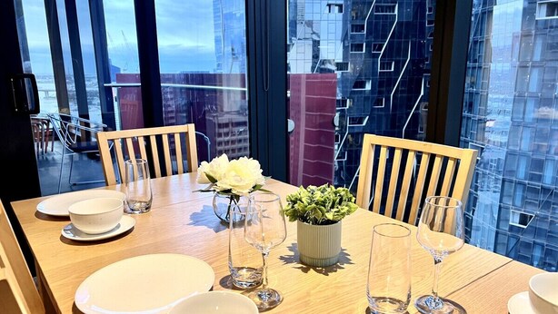 A dining table set for four with white plates, bowls, and glasses, and a potted plant in the center.