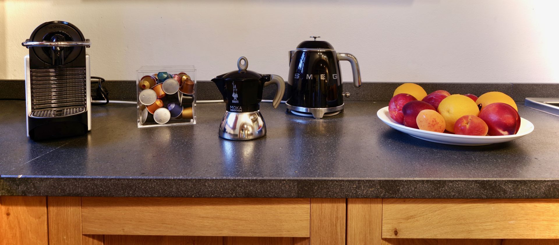 Een keukenblad met een koffiezetapparaat, een waterkoker en een schaal fruit.