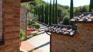 A stone pathway leading through a garden with tall trees and colorful flowers. - Vivaia Arceno Rentals Club, Villa in Chianti , Exclusive Pool Concierge Freewifi (San Gusmè)