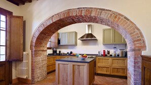 A kitchen with a brick archway, wooden cabinets, a central island, and a stainless steel range hood. - Vivaia Arceno Rentals Club, Villa in Chianti , Exclusive Pool Concierge Freewifi (San Gusmè)