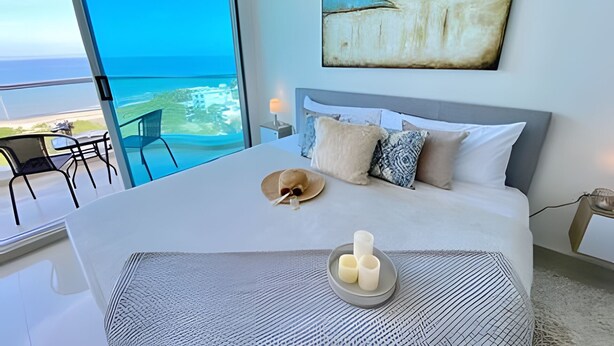 A bedroom with a large bed, a view of the sea, and a painting on the wall. - Apartamentos Aragoa - Cerca al Mar by SOHO (Santa Marta)