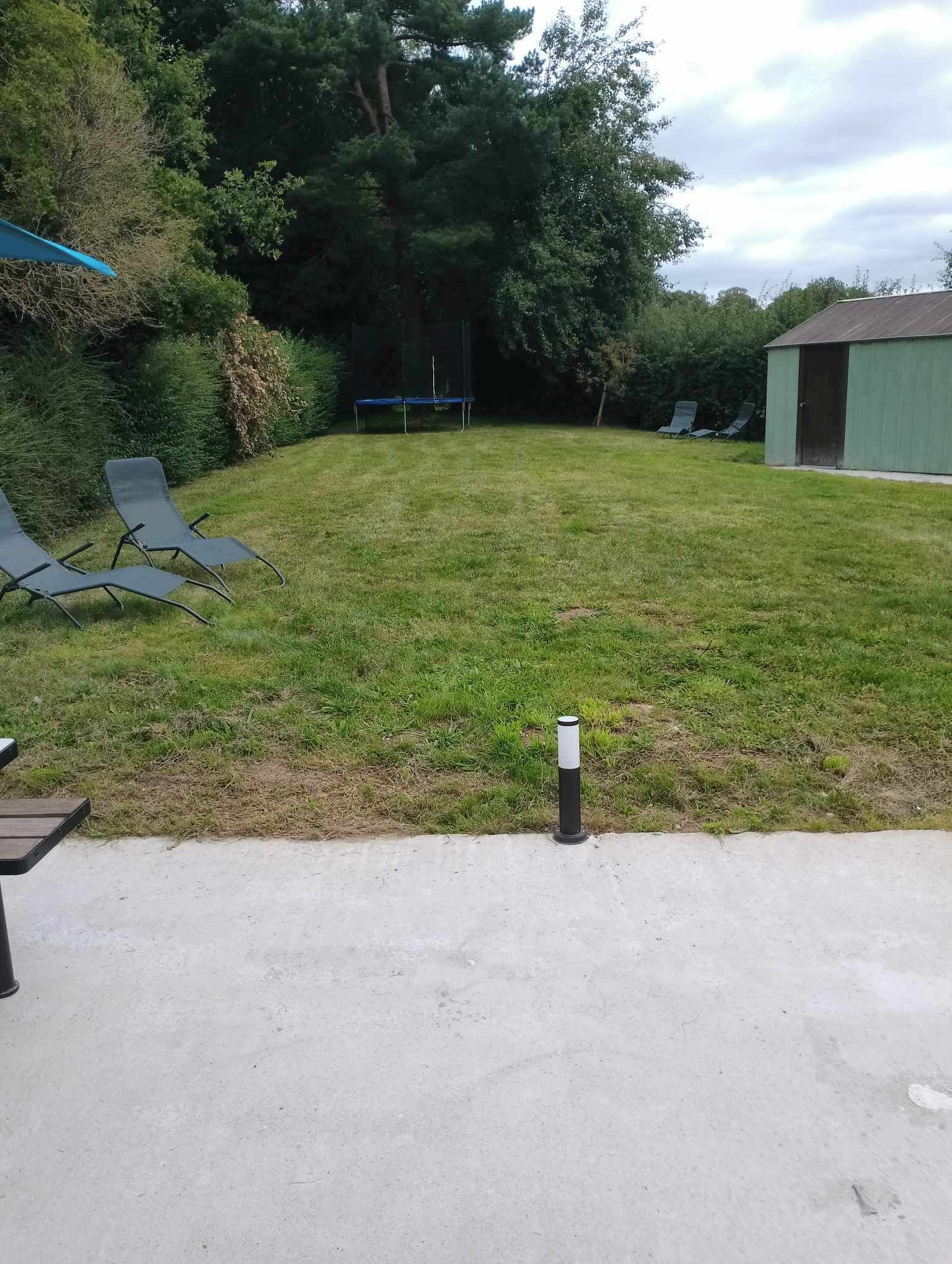 Een gazon met een trampoline, lounge stoelen en een tuinhuis.