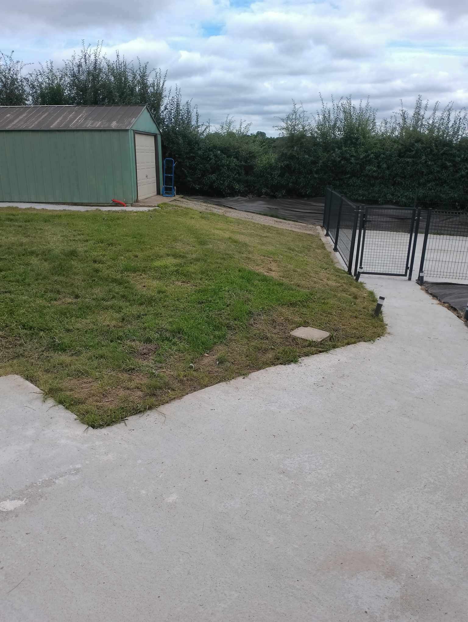 A grassy area with a concrete path leading to a fenced area.