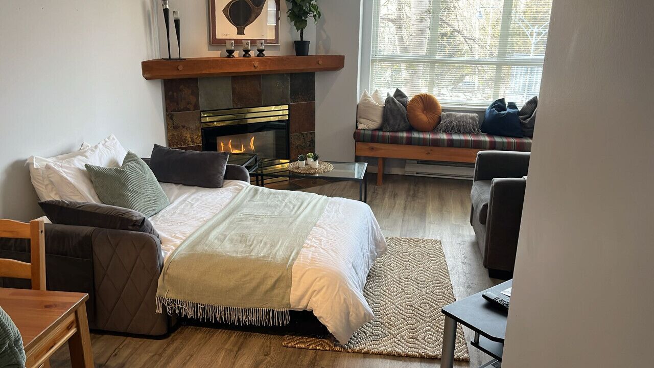 A cozy living room with a fireplace, a sofa with cushions, a coffee table, and a TV.