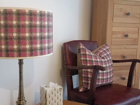 Una habitación con una lámpara escocesa, un sillón de cuero con un cojín a cuadros, y un mueble de madera con cajones.