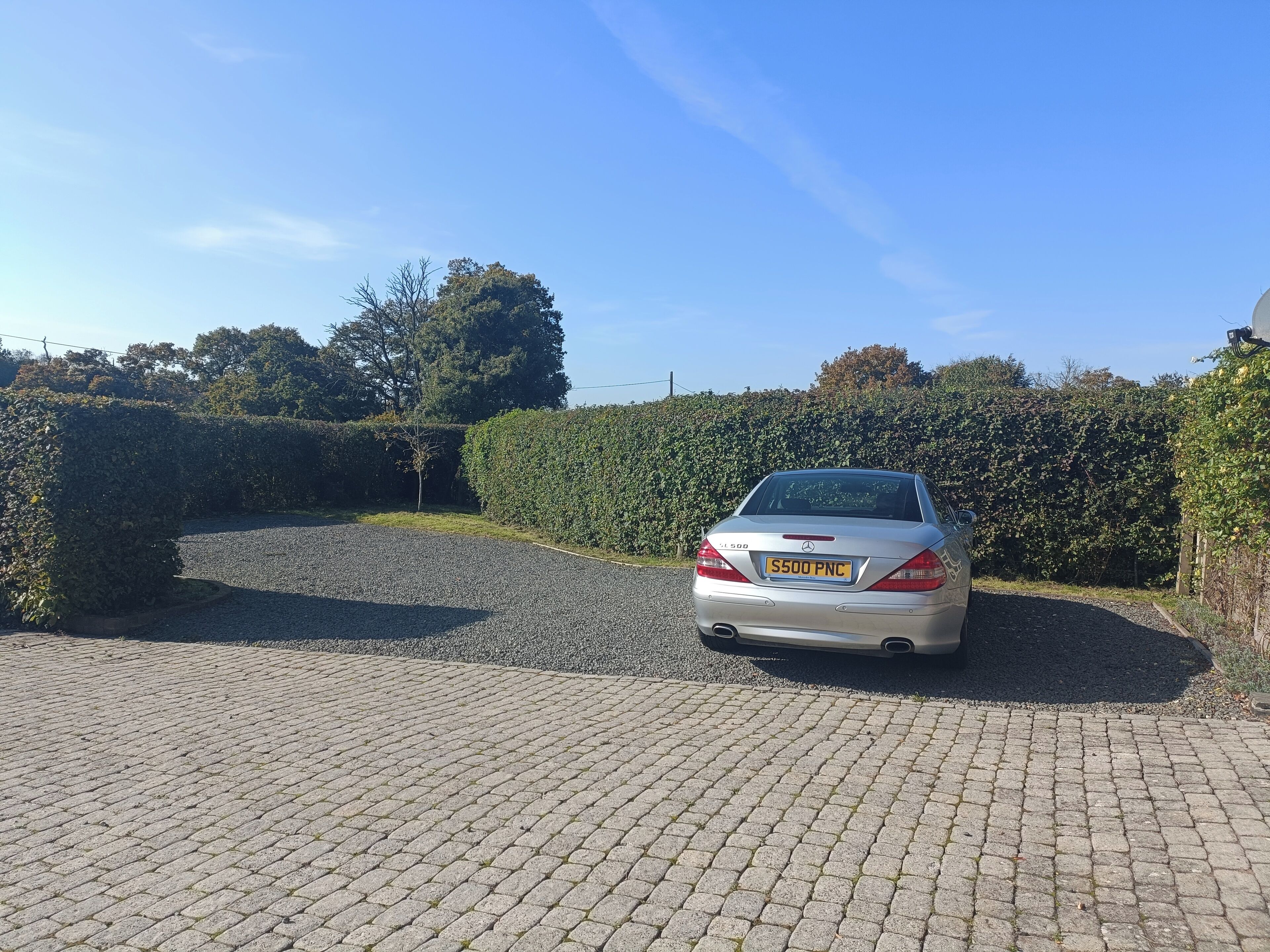 Een zilveren auto geparkeerd op een verharde oprit, met een haag en bomen op de achtergrond.