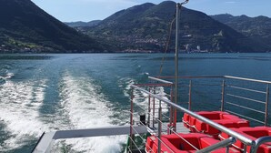 A boat with red seating and metal railings, moving on a body of water with mountains in the background.