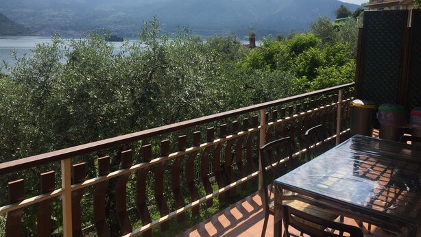A balcony with a glass table and chairs, overlooking a lake and mountains.