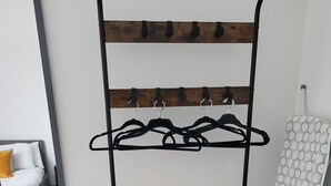 A metal rack with multiple hangers and a wooden shelf, a mirror, and a white ironing board with a hexagonal pattern. - Best Priced Apartment In Danum  19 (Doncaster)