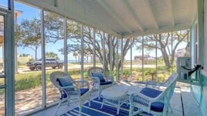 Un espace extérieur aménagé, abrité et doté de chaises en osier et d’une table, offrant une vue sur une plage et un parking.