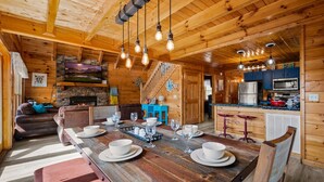 A wooden interior with a dining table set for six, a kitchen area, and a living room with a fireplace.