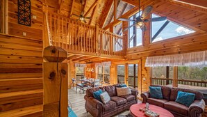 A spacious wooden cabin with a loft bedroom, a dining area, and a cozy living room with leather sofas and a red coffee table.